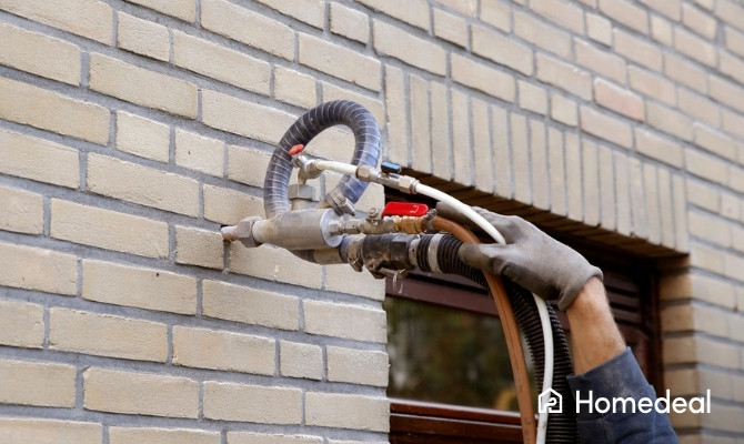 Vakman brengt isolatiemateriaal aan in een spouwmuur van een bakstenen gevel.