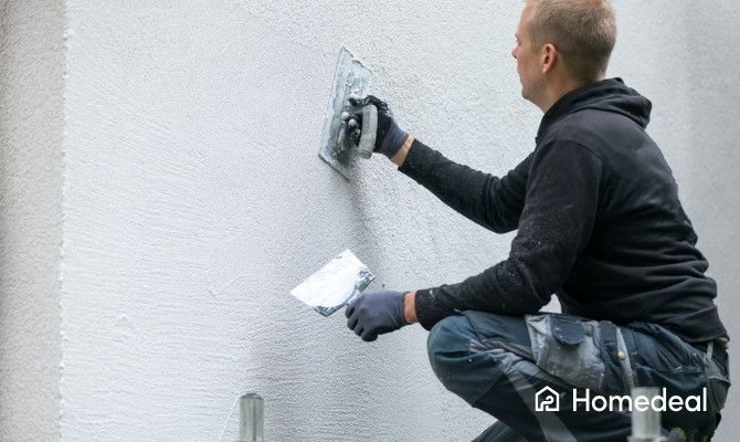 Stukadoor aan het werk met een spaan, bezig met het bezetten van een buitenmuur met pleisterwerk.