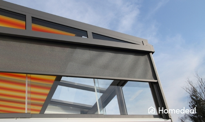 ritsscreen zonwering op een moderne glazen gevel met strak grijs doek en aluminium frame, onder een helderblauwe lucht.