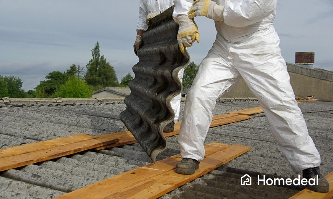 Asbestspecialisten in beschermende kleding verwijderen asbesthoudende golfplaten van een dak.