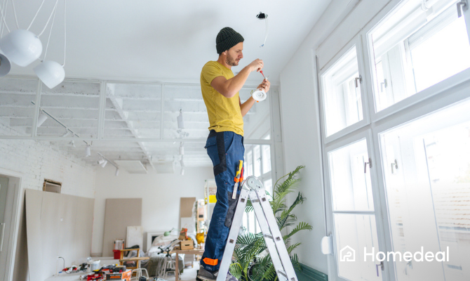 Elektricien staat op een trap en installeert verlichting - een plafondspot
