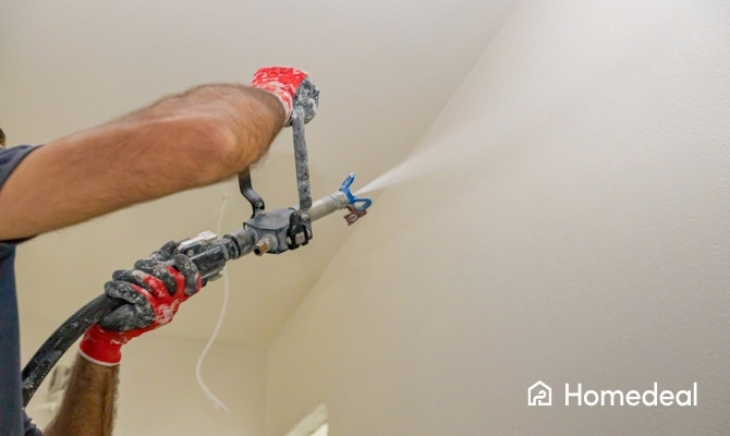 Vakman brengt spackspuitwerk aan op het plafond met een spuitmachine, een snelle en goedkope manier van wand- en plafondafwerking.