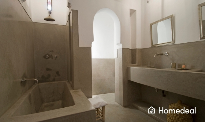 Minimalistische badkamer in Marokkaanse stijl met tadelakt afwerking, ingebouwd bad, dubbele wastafel en boogvormige doorgang.