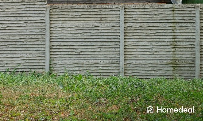 Betonnen schutting met horizontale betonpanelen en omgeven door groen.