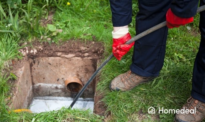 Medewerker van een ontstoppingsdienst reinigt een verstopte afvoer in de tuin met professioneel ontstoppingsgereedschap.